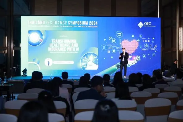 วิทยากรยืนบนเวทีหน้า Presentation เรื่อง Transforming Healthcare and Insurance with AI